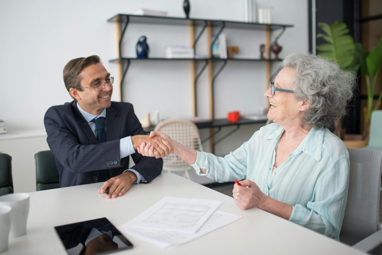 A man and woman shaking hands over papers.